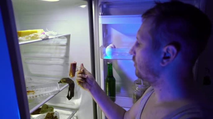 在冰箱里找食物的人。未刮胡子的人在冰箱里挖东西，尝试剩菜并关闭。