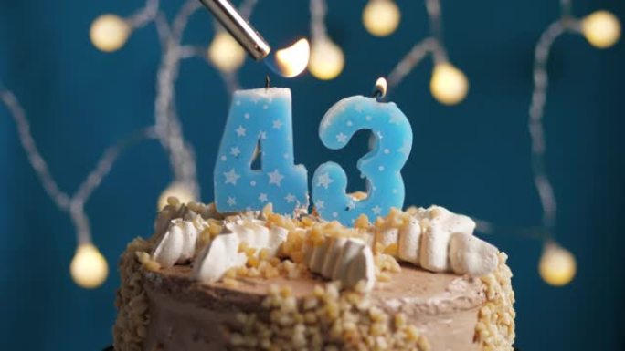 蓝色背景上有43个数字蜡烛的生日蛋糕。蜡烛着火了。慢动作和特写视图