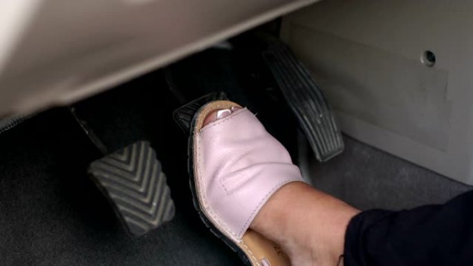 一个女人穿着夏天的鞋子的特写镜头在汽车上踩下了制动踏板。