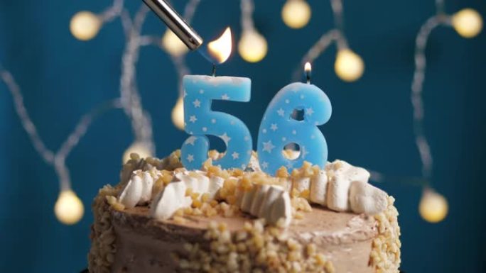 蓝色背景上有56号蜡烛的生日蛋糕。蜡烛着火了。慢动作和特写视图