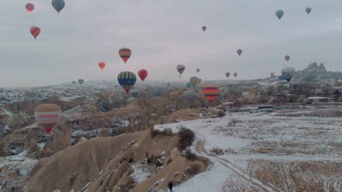 卡帕多西亚日出时，五颜六色的热气球在白雪皑皑的童话烟囱上