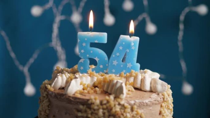 蓝色背景上有54号蜡烛的生日蛋糕。蜡烛吹灭了。慢动作和特写视图