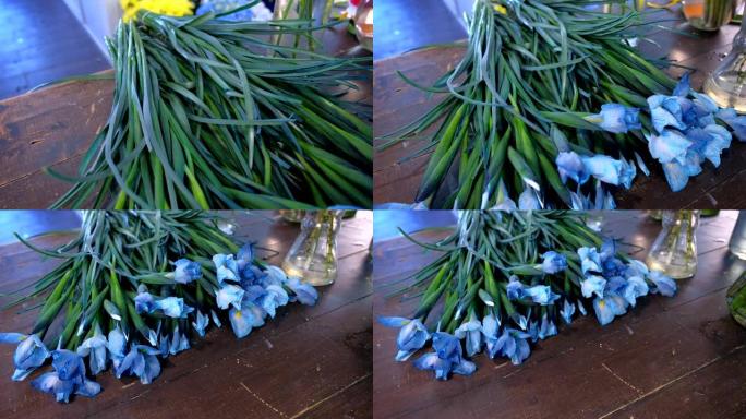 在花店的深色木制桌子上，蓝色可爱的鸢尾花长茎。