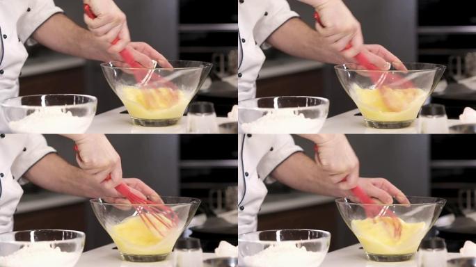 厨师积极地在透明的盘子里鞭打鸡蛋。在厨房里煮煎蛋卷