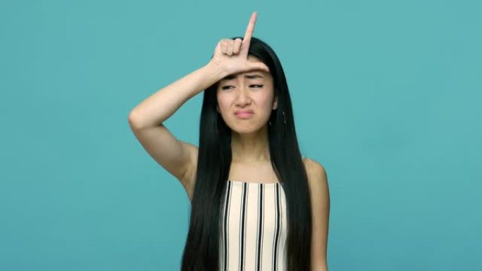我是失败者。悲伤的绝望的亚洲女人，留着长长的黑发，在她的前头上显示失败者的手势，带着悲伤的紧张不快乐