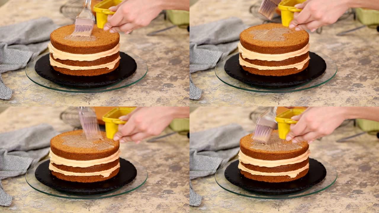 无法辨认的女性糖果手在厨房用硅烹饪刷用甜焦糖糖浆浸泡海绵蛋糕，特写。