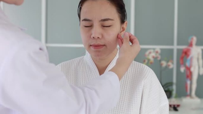 医生进行针灸治疗的手。在诊所医院接受针灸治疗的亚洲女性用细针插入面部皮肤
