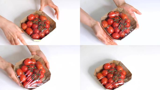 女人用食物薄膜在白色桌子上储存食物。包装产品用透明聚乙烯食品薄膜卷。樱桃番茄在一次性塑料包装慢动作视