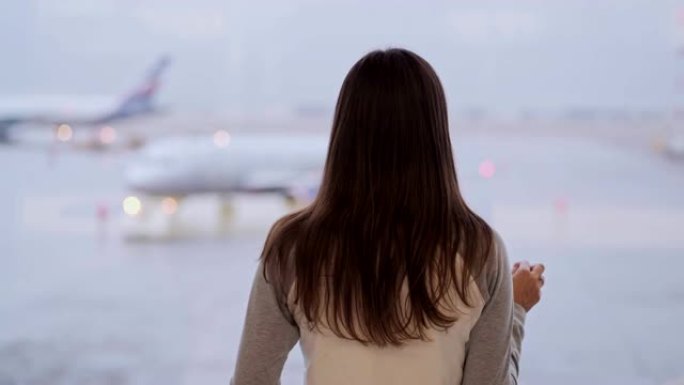 站在机场航站楼的女人的背面视图，看着窗外的飞机