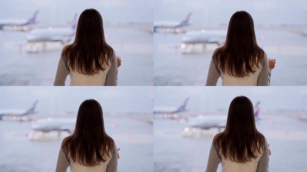 站在机场航站楼的女人的背面视图，看着窗外的飞机