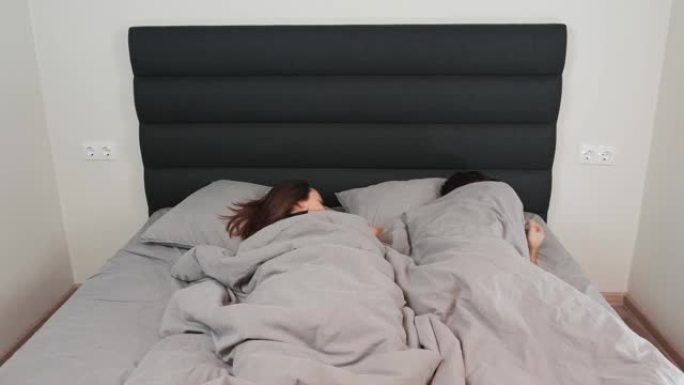 年轻的家庭夫妇睡在床上，时光倒流。女人和男人躺在灰色的床上，闭着眼睛。已婚夫妇睡在家里的床上，时间流