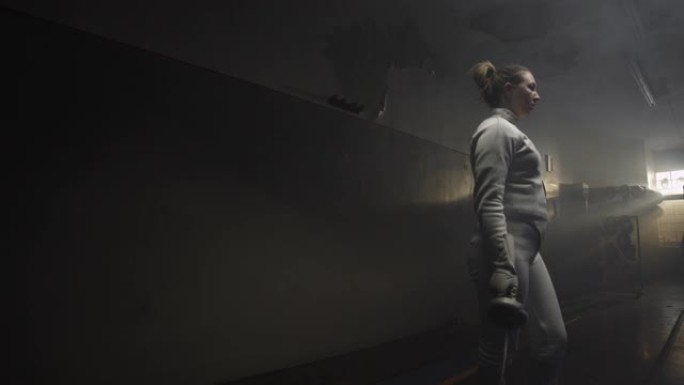 在黑暗多雾的训练馆中，一名女子击剑运动员的肖像