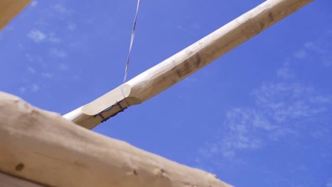 起重机在蓝天背景上举起横梁。夹。建筑工地的起重机将经过处理的重型木材抬到建筑工地