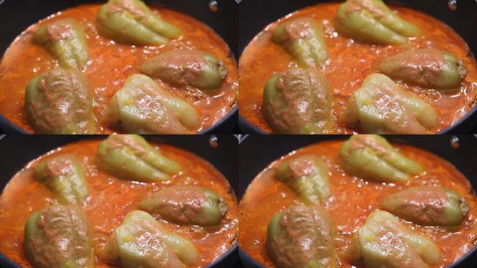 塞满肉末的彩色辣椒在炉子上的平底锅里炖。在厨房里烹饪美味的食物特写。
