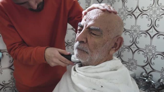 非常老的土耳其穆斯林祖父在他设计1980年的老式浴室里被孙子修剪眉毛