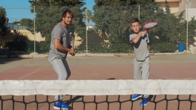 打网球的孩子。父亲和儿子在coart上练习网球。一起积极休闲