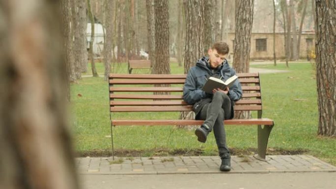 年轻的大胡子男人在秋季公园读完一本书，从长凳上站起来，离开其他地方。阅读概念