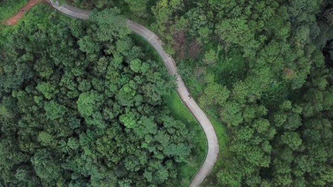 在泰国清莱府高地山脉的绿色森林中，一辆摩托车在道路上行驶的鸟瞰图。