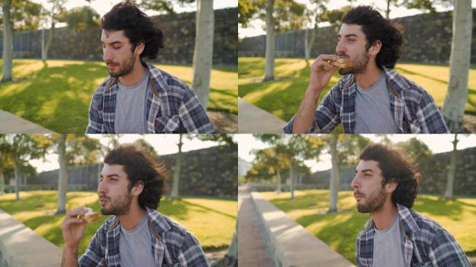 在炎热的夏日里，饥饿的英俊年轻人坐在公园里吃三明治的特写镜头