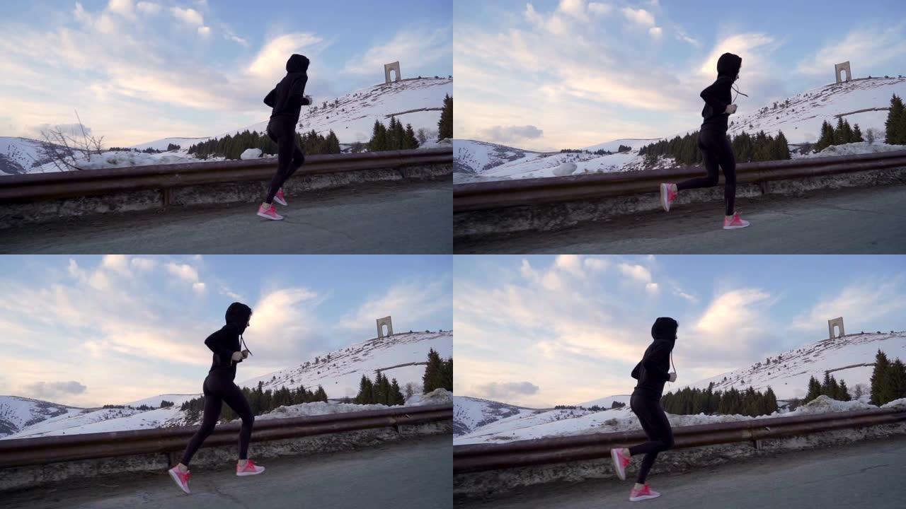 年轻的健身女子在雪地里慢跑。背景中的自由弧，日落时彩云