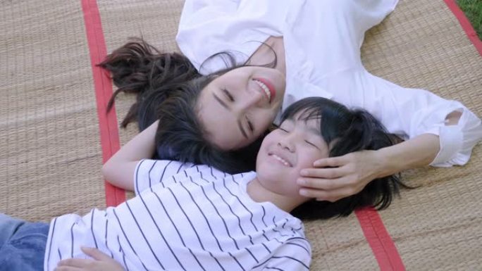 亚洲年轻的母亲和儿子躺在房子前的草坪上，看着彼此相爱的笑脸