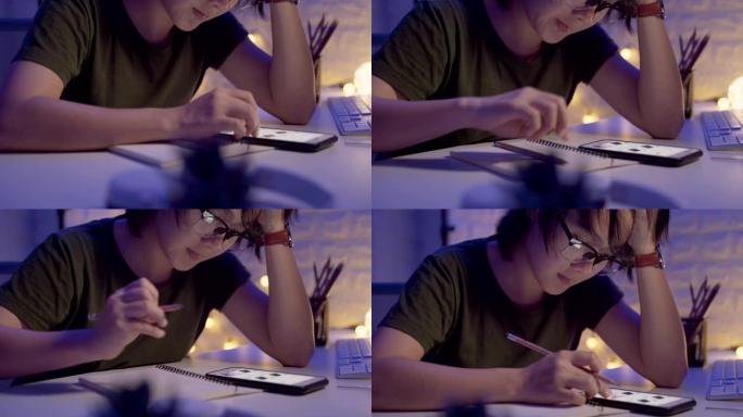 亚洲女人在笔记本上写字，晚上使用智能手机。移动相机视差效果。