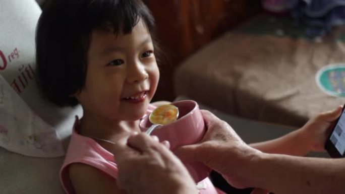 小女孩亚洲人在家里用智能手机吃饭