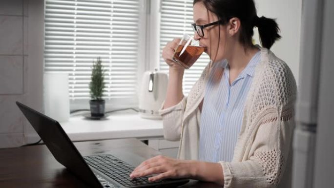 自由职业者，程序员，编码员，黑客，通信社交网络概念。戴眼镜的迷人女人在厨房工作，看着笔记本电脑屏幕，