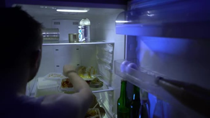 在冰箱里找食物的人。未刮胡子的人在冰箱里挖东西，他拿披萨。