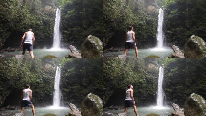 站在瀑布脚下的男性游客对大自然的景色感到惊讶。