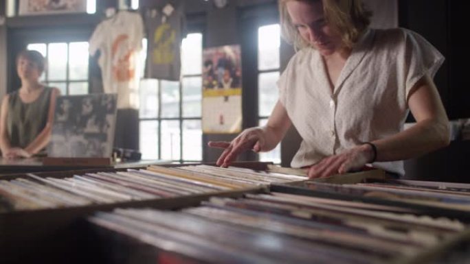 一名年轻女子在唱片店中筛选黑胶唱片时跳舞，背景是女店员