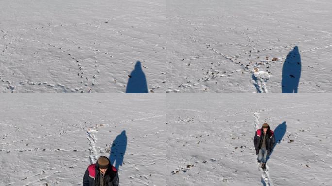在冬天阳光明媚的日子里，穿着牛仔裤和保暖鞋的男人在雪原上行走。从上方鸟瞰图