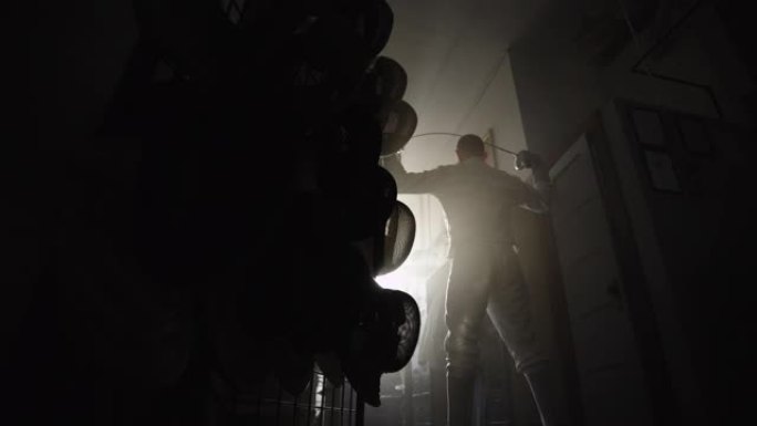 一名男子击剑手站在尘土飞扬的设备储物柜中，用击剑箔纸伸展