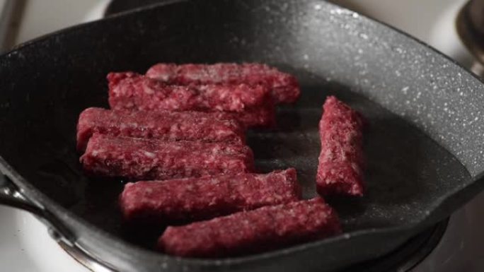 男子将盐和胡椒粉放在新鲜的红肉烤肉串上，用热油将其放入煎锅中，以在家庭厨房中炸午餐。