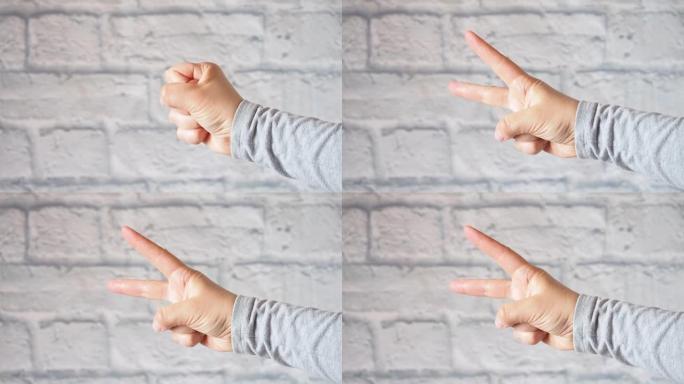 女人的手两个手指指向侧面。灰色砖墙。复制空间