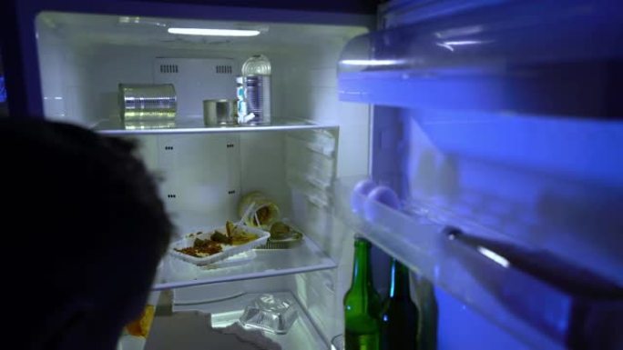 在冰箱里找食物的人。那家伙从冰箱里拿披萨和一瓶啤酒。