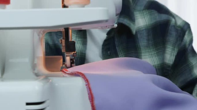 裁缝在车间用缝纫机缝制衣服。包锁机的细节。在裁缝工作室工作和制作服装的女人的手的特写。创作和剪裁服装