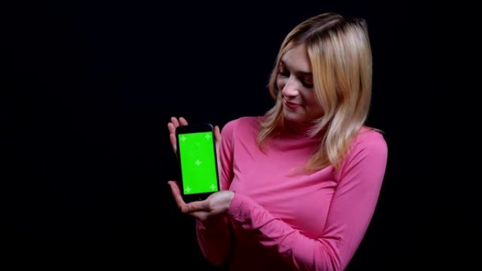 使用手机拍摄年轻漂亮的金发女性的特写镜头，并显示绿屏，适用于背景隔离在黑色的相机
