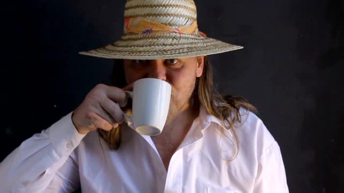 一个穿着白衬衫，戴着女性化草帽的长发的胖子，黑底留着胡须，吃白面包，喝白色杯子里的咖啡