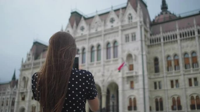 女孩在匈牙利布达佩斯的国会大厦拍摄手机照片