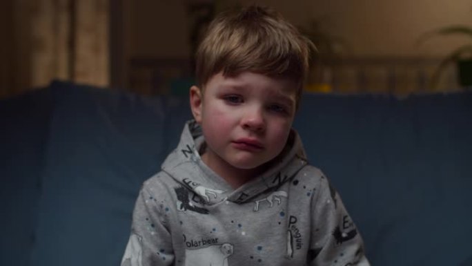 年轻哭泣的男孩坐在家里的沙发上的肖像。非常沮丧的孩子的脸看着镜头慢动作。