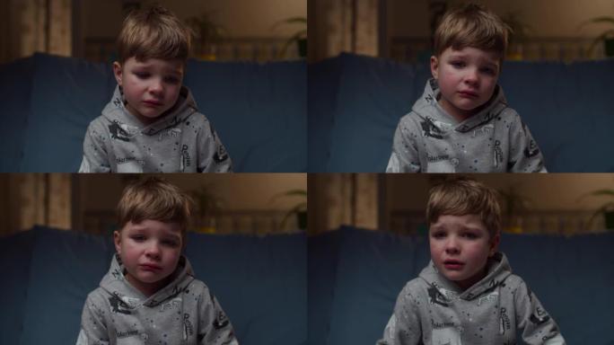 年轻哭泣的男孩坐在家里的沙发上的肖像。非常沮丧的孩子的脸看着镜头慢动作。