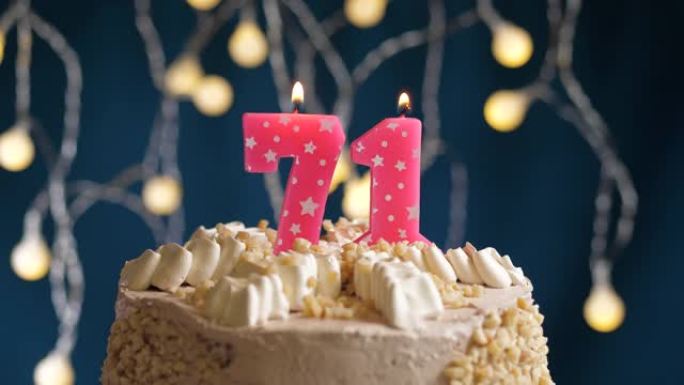 蓝色背景上有71号粉色蜡烛的生日蛋糕。蜡烛吹灭了。慢动作和特写视图