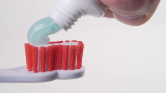 一只手用刷毛的水龙头将蓝色牙膏从管子上挤到白色塑料牙刷上特写