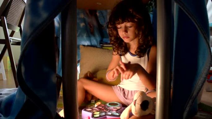 一个漂亮的孩子女孩正在桌子FDV下的一个巢穴里用奶油照顾她的手