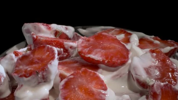 黑色背景上覆盖着厚厚的奶油的新鲜草莓的慢动作旋转。相机旋转360度，特写。