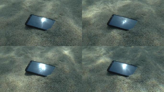 智能手机位于屏幕上塌陷的海床上，用光线反射太阳，用小波反射蓝色的水面。水下视图。地中海，欧洲。