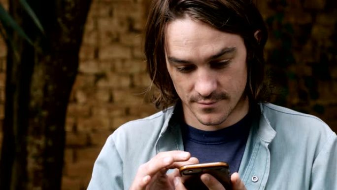一个20多岁或30多岁的英俊年轻人使用智能手机的特写