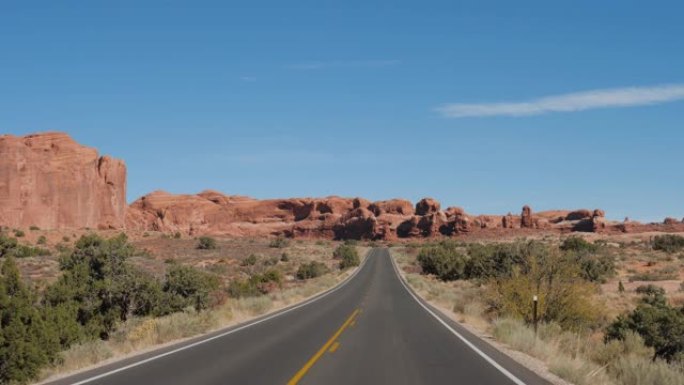 在空旷的道路上行驶，穿过美国沙漠中带有红色岩石地层的拱门公园