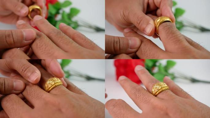 女人在情人节把金色订婚戒指放在男人的手上，订婚夫妇的手和红色玫瑰花束背景上的金戒指。